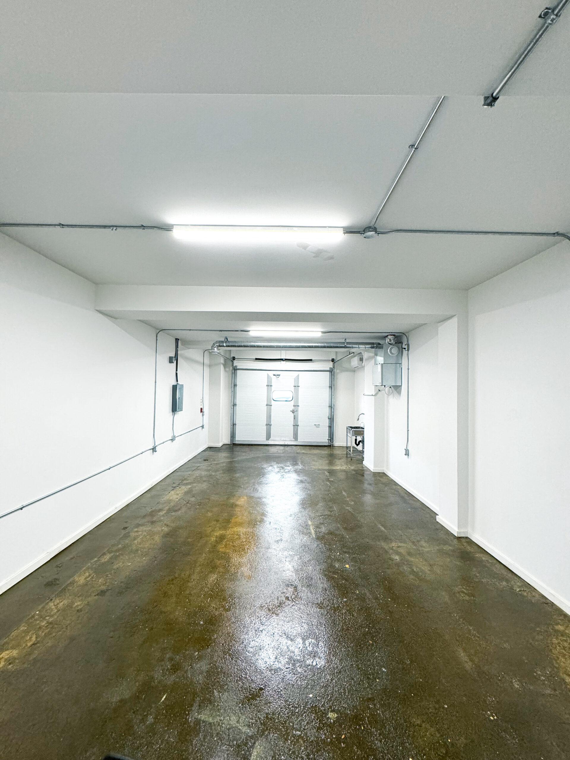 Lower Studio_1A Clean empty workshop space looking at the closed garage door